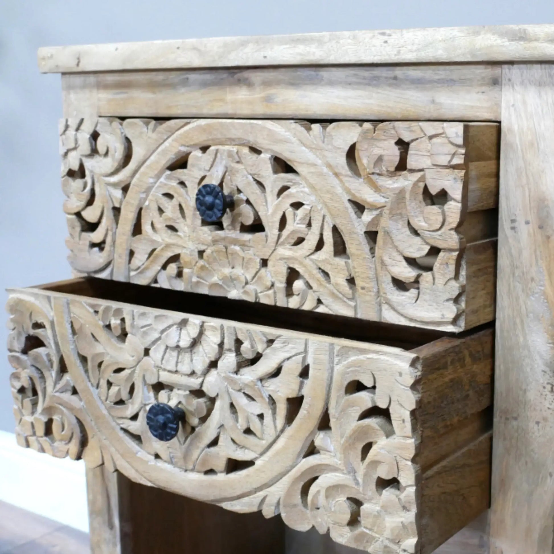 Wooden drawer with intricate carvings and dark knobs on a light background