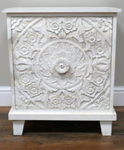 White ornate cabinet with floral patterns on a wooden floor.