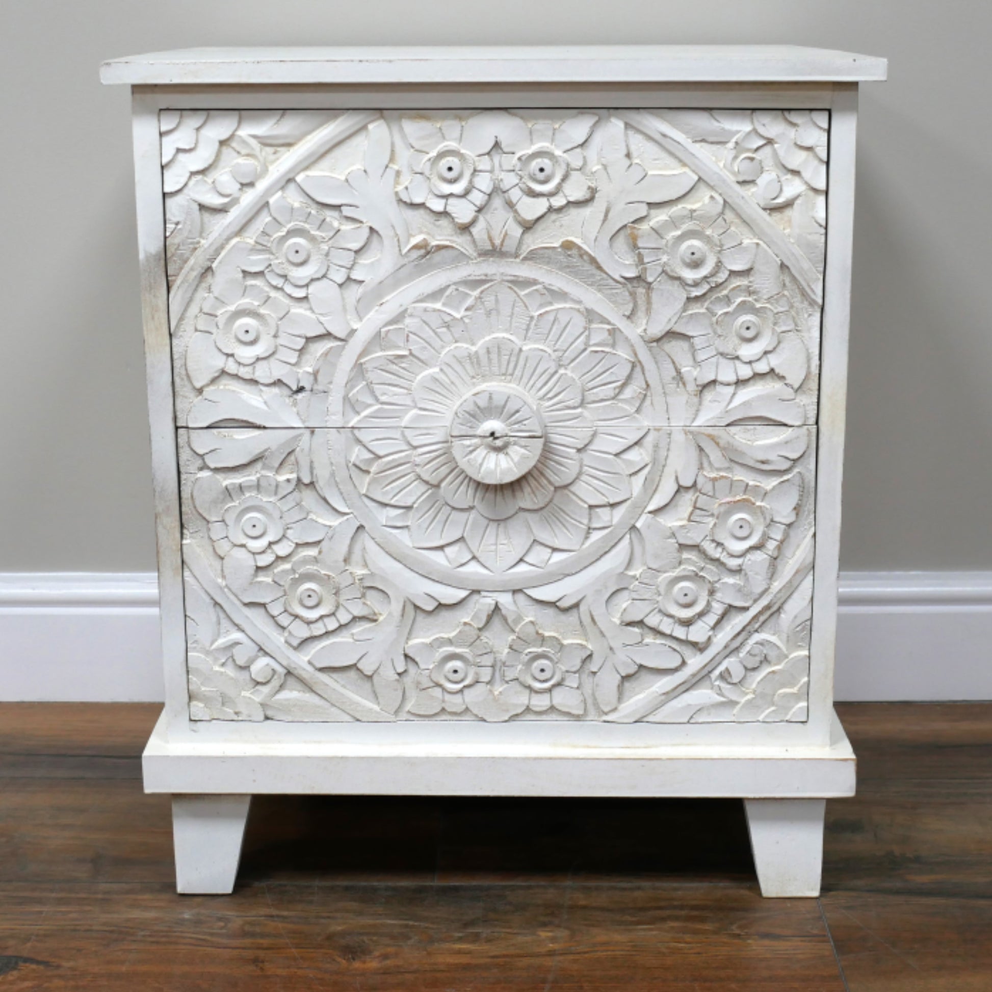 White ornate cabinet with floral patterns on a wooden floor.