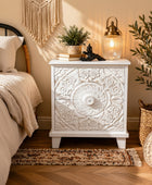 Decorative white nightstand with intricate carvings in a bedroom setting.