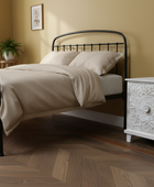 Bedroom with a black metal bed and white nightstand against a beige wall.