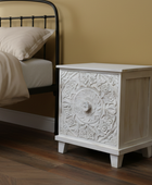 Decorative nightstand with intricate carvings next to a bed in a bedroom setting.