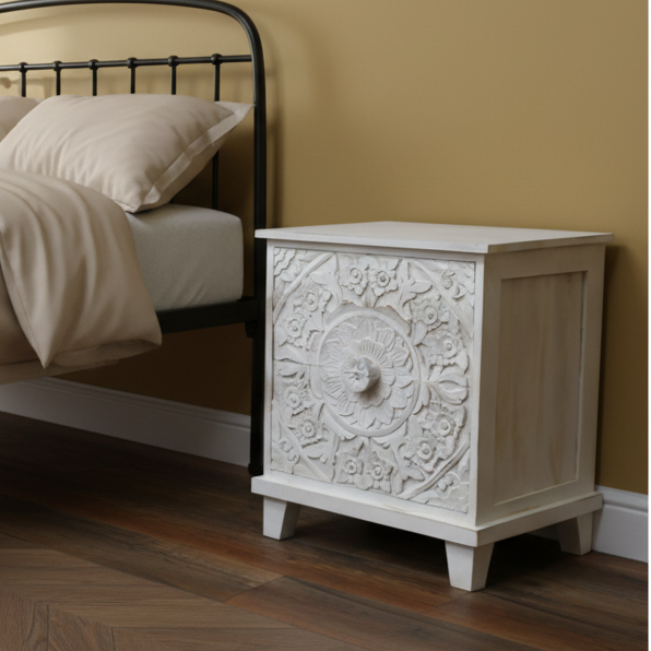 Decorative nightstand with intricate carvings next to a bed in a bedroom setting.