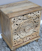 Wooden side table with intricate carvings on a gray rug against a light blue wall.