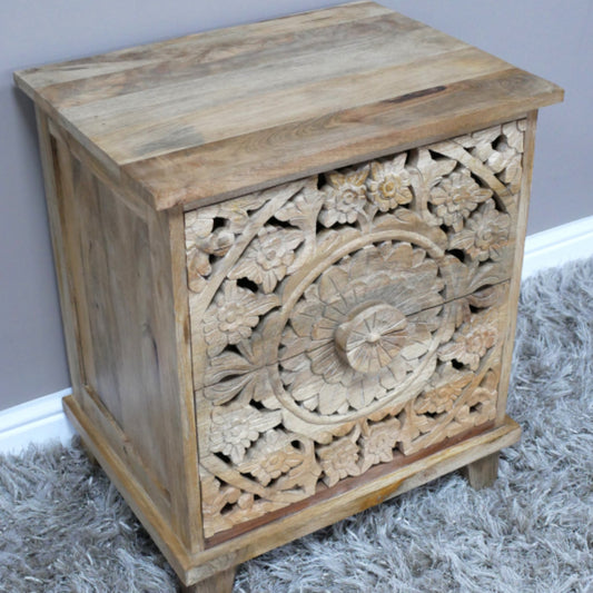 Wooden side table with intricate carvings on a gray rug against a light blue wall.
