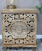 Wooden side table with intricate carvings and a lamp on top, against a neutral background.