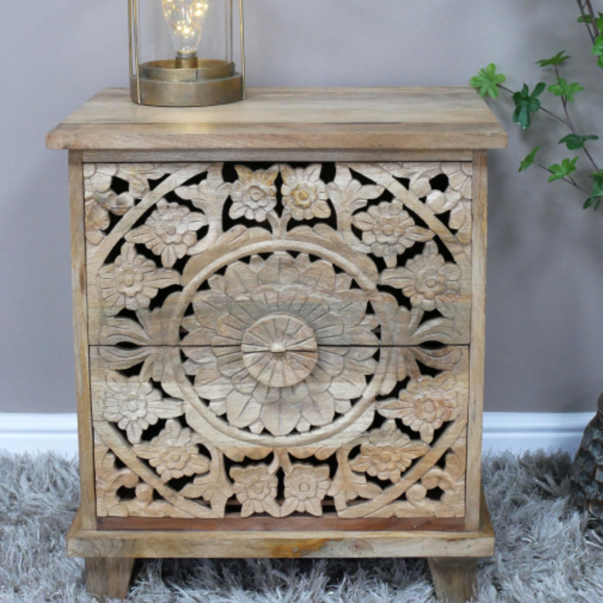 Wooden side table with intricate carvings and a lamp on top, against a neutral background.