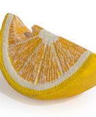 A ceramic sculpture shaped like a stylized orange slice, featuring textured yellow-orange segments, a thick yellow rind, and a white pith center, displayed on a clean white background.