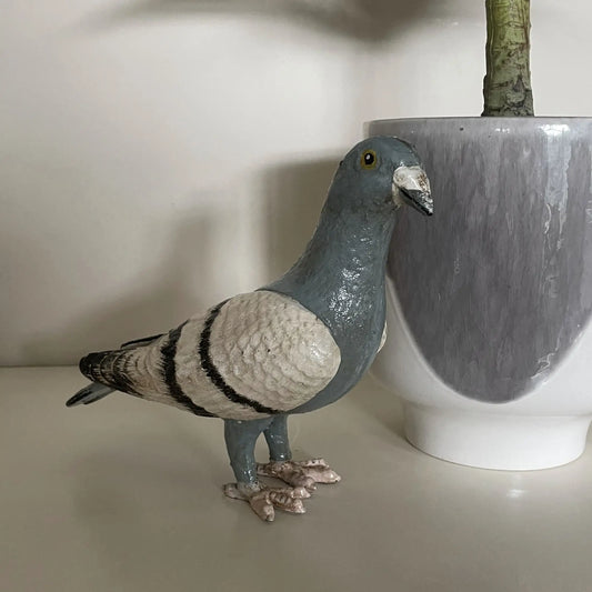 Statue of a pigeon next to a pot on a light surface