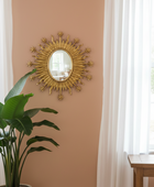 Gold sunburst mirror on a beige wall with a plant and table in the foreground