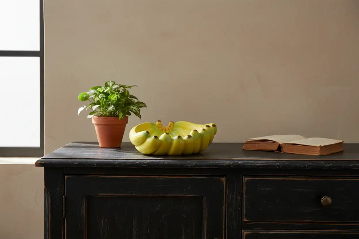 Bowl of fruit, potted plant, and open book on a wooden surface with a neutral background