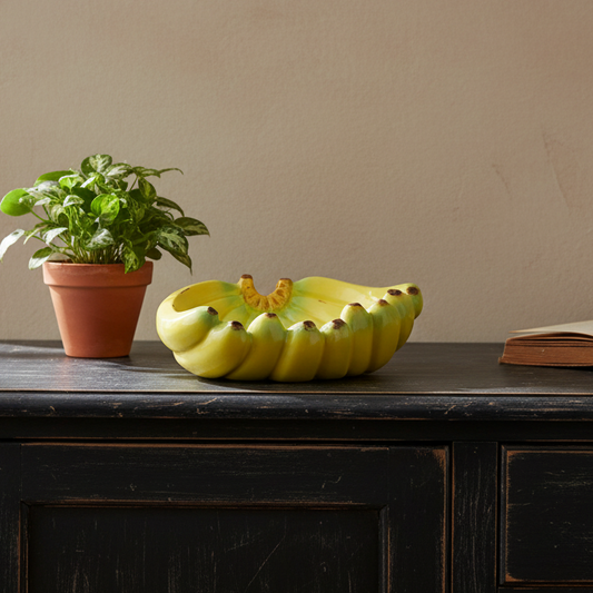 Decorative fruit bowl shaped like a banana on a wooden surface with a plant and book in the background.