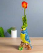 Colorful parrot figurine with a tulip on a wooden surface against a gray wall.