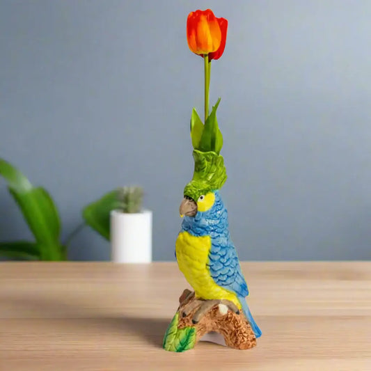Colorful parrot figurine with a tulip on a wooden surface against a gray wall.