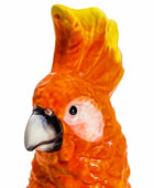 Close-up of a ceramic parrot figurine with orange and yellow feathers on a white background
