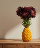 Pineapple-shaped vase with flowers on a wooden surface