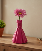 Pink dress-shaped vase with a single pink flower on a wooden surface.
