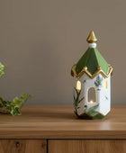 Decorative lantern with green roof and gold accents on a wooden surface next to a plant.