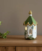 Decorative lantern with green roof and gold accents on a wooden surface.