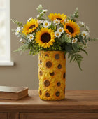 Decorative vase with sunflower pattern containing a bouquet of sunflowers and daisies on a wooden surface.