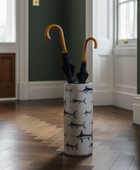 A tall white umbrella stand with a navy blue shark pattern, holding two closed umbrellas with curved wooden handles, set in a hallway with dark green walls and a wood floor.