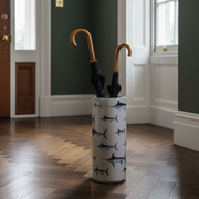 A tall white umbrella stand with a navy blue shark pattern, holding two closed umbrellas with curved wooden handles, set in a hallway with dark green walls and a wood floor.
