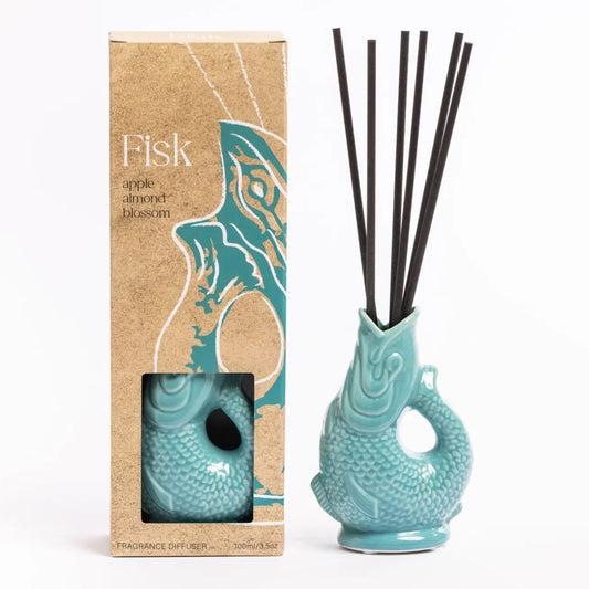 A reed diffuser set with a turquoise fish-shaped ceramic diffuser vase containing black reeds, shown next to its kraft paper packaging box labeled 'Fisk' on a white background.