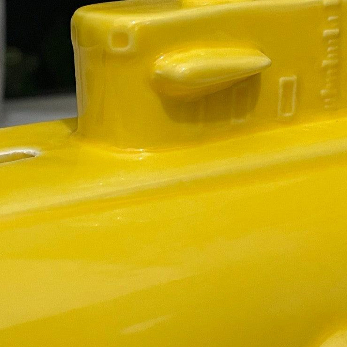 Close-up of a glossy bright yellow object, showing part of a raised molded section with a small protruding tab and embossed details.