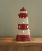 Red and white lighthouse-shaped lamp on a wooden surface with a plant in the background.