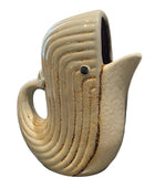 A ceramic whale-shaped pitcher with a cream-colored glaze and brown textured streaks, set on a dark granite countertop in a kitchen environment.
