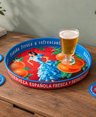 A round decorative serving tray with a colorful Spanish-themed illustration, placed on a rustic wooden table. The tray features a red background with orange fruits, green leaves, a woman in a blue dress, and blue rim accents.