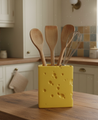 Yellow cheese-shaped utensil holder with wooden spoons on a kitchen counter.