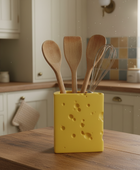 Yellow cheese-shaped utensil holder with wooden spoons and a whisk on a kitchen counter.