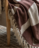 Brown and beige checkered blanket with tassels draped over a wooden chair.