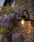 Outdoor wall light fixture on a stone wall with wisteria plants.