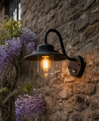 Wall-mounted outdoor light fixture on a stone wall with wisteria plants.
