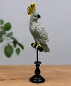 Gray parrot figurine with a yellow crest on a black stand against a white background