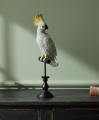 Decorative cockatoo figure on a stand with a plant and book in the background