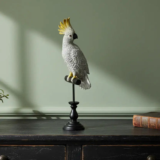 Decorative parrot sculpture on a stand against a green wall