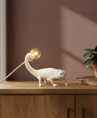 Lamp shaped like a chameleon on a wooden surface with a plant in the background