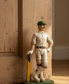 Statue of a cricket player holding a bat against a wooden wall.