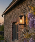 Stone building with a light fixture and wisteria flowers at dusk.