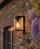 Outdoor wall light fixture on a stone wall with wisteria flowers in the foreground