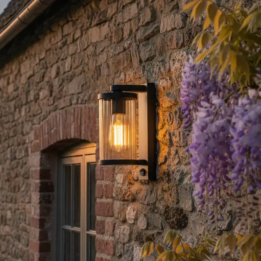 Outdoor wall light fixture on a stone wall with wisteria flowers in the foreground