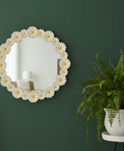 Decorative mirror with floral design on a green wall next to a potted fern.