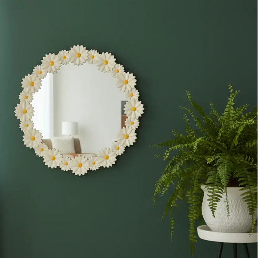 Decorative mirror with floral design on a green wall next to a potted fern.