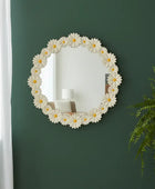 Round floral mirror with white flowers and yellow centers on a green wall.