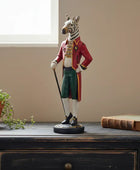 Statue of a zebra in formal attire on a wooden surface with a plant and book in the background.