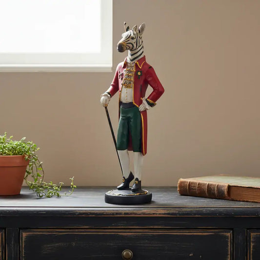 Statue of a zebra in formal attire on a wooden surface with a plant and book in the background.