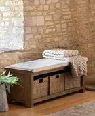 Wooden bench with storage baskets and folded blankets against a stone wall.